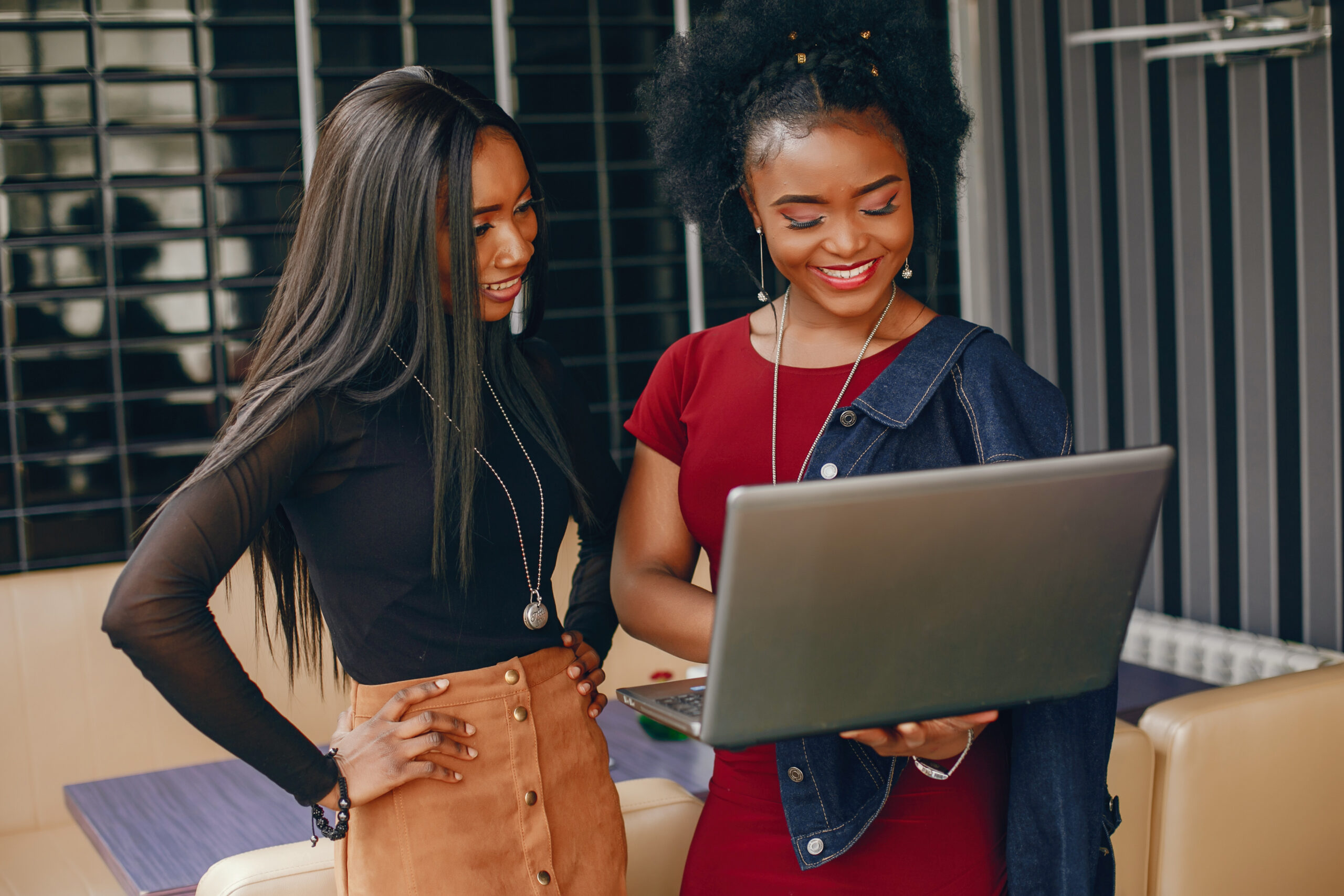 two beautiful and stylish young, dark girls standing in a restaurant and using a laptop